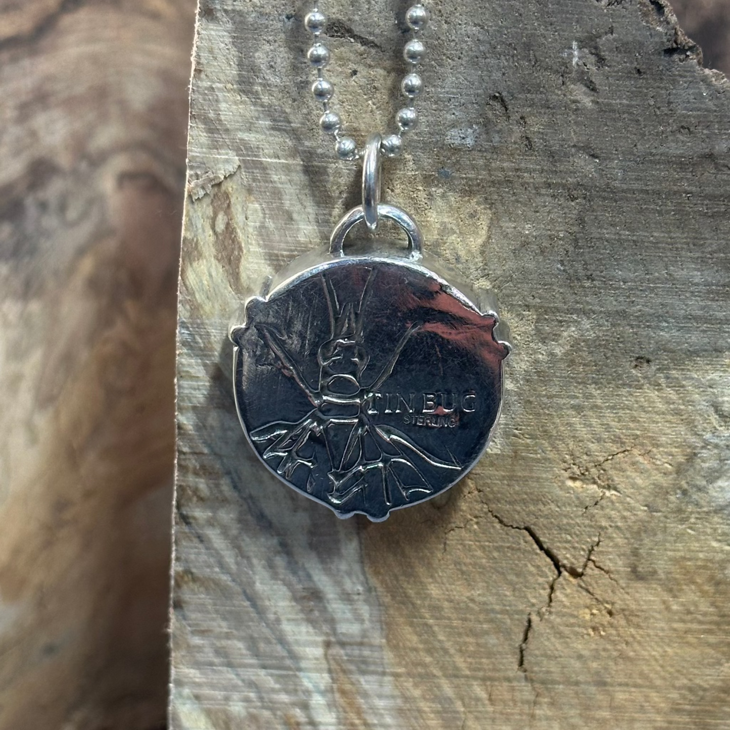 Back side of 1" round sterling silver pendant on ball chain stamped with Tin Bug logo and STERLING and embossed with a lacewing bug