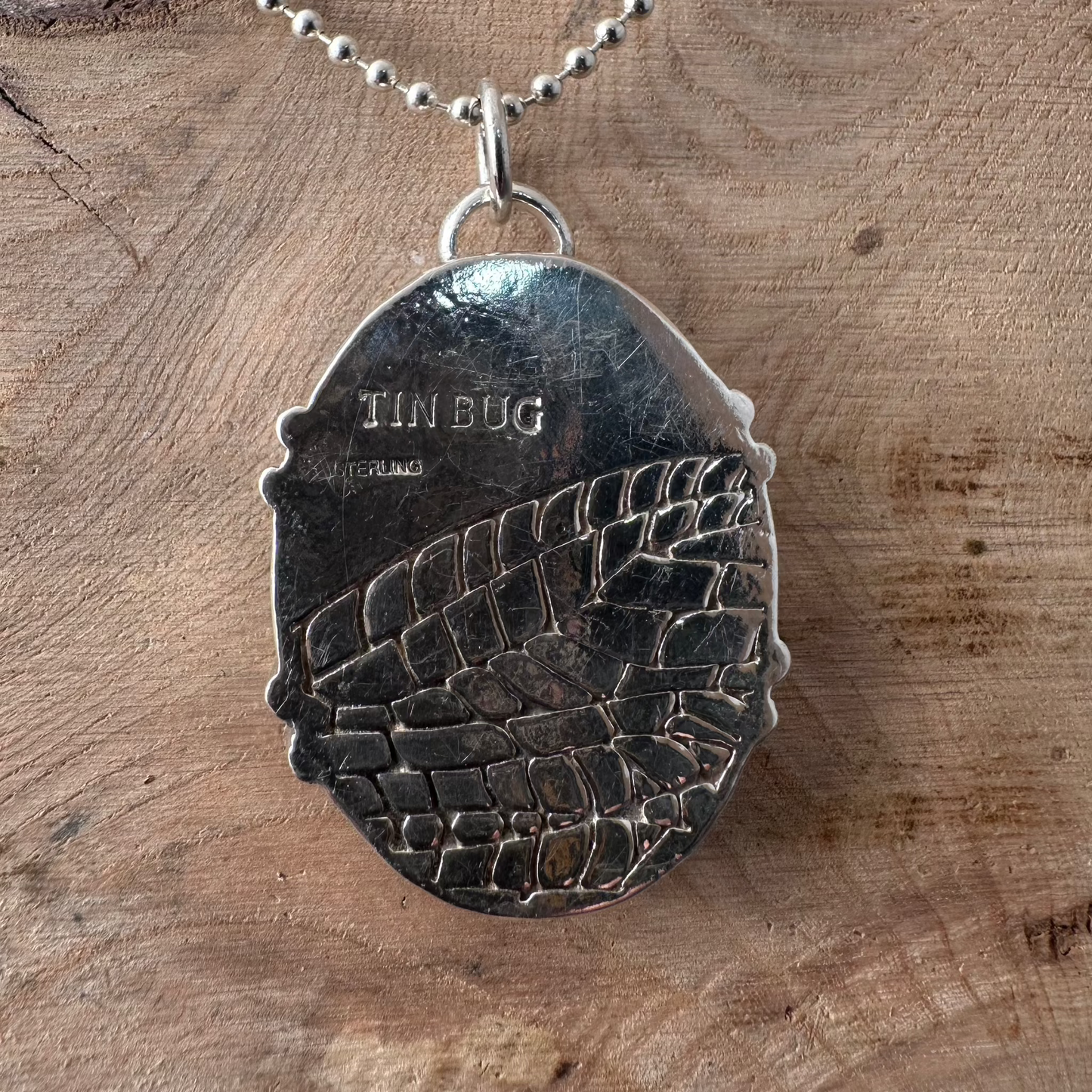Back side of 1.625"x1.25" oval recycled sterling silver mosaic pendant on ball chain stamped with Tin Bug logo and STERLING and embossed with the wing of a lacewing