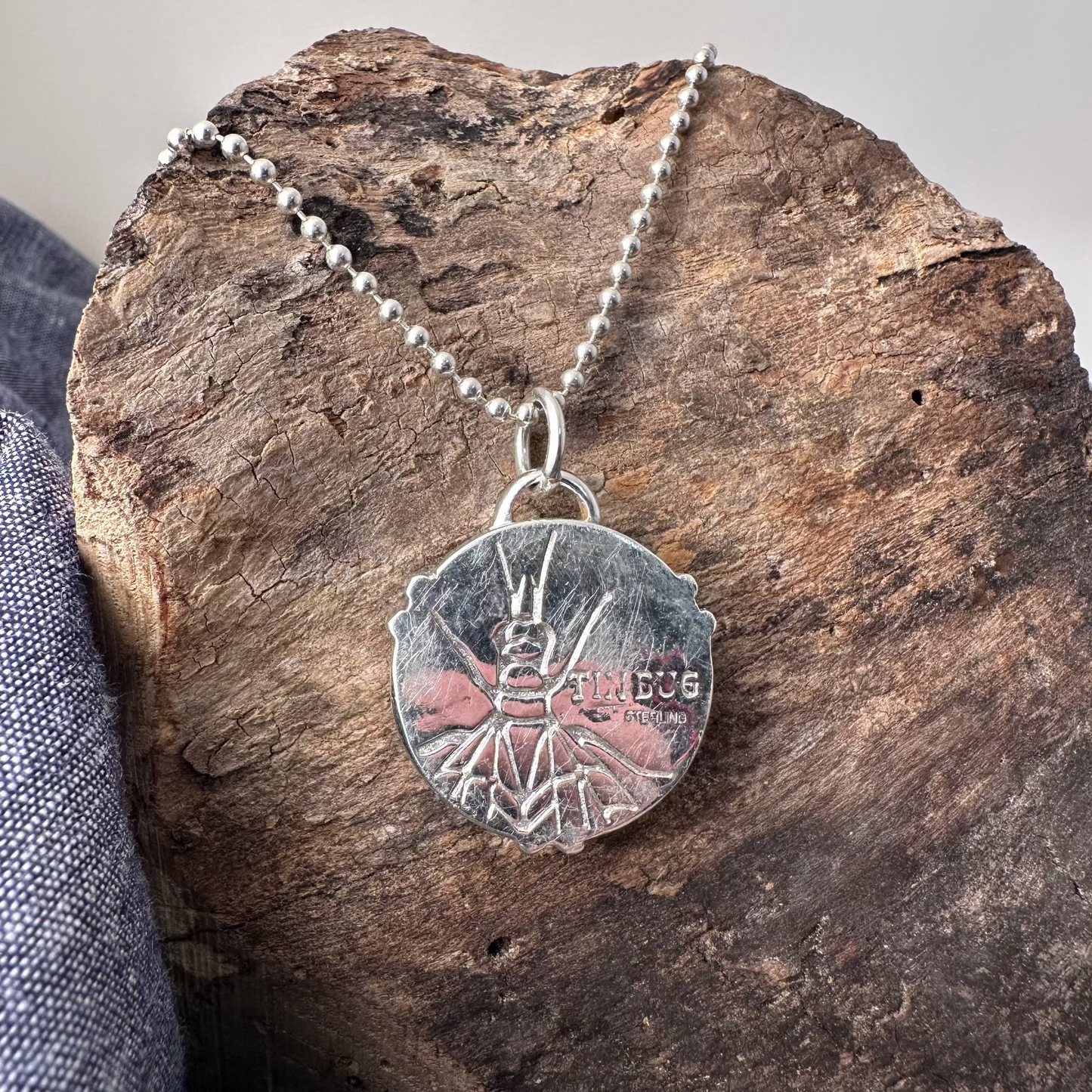 Back side of 1" round sterling silver pendant on ball chain stamped with Tin Bug logo and STERLING and embossed with a lacewing bug.